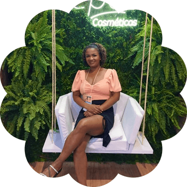 Jucelia Pereira, ex-técnica de enfermagem que transformou sua vida ao fundar uma loja de cosméticos, sentada em um balanço cercada por folhagens.